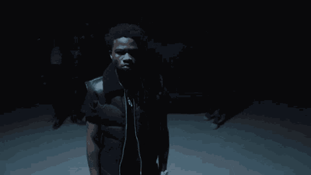 a man wearing a black vest and headphones stands in the dark