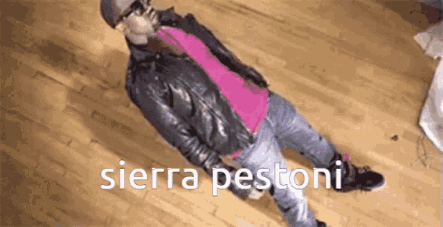 a man in a leather jacket and pink shirt is laying on a wooden floor with the words sierra pestoni written below him