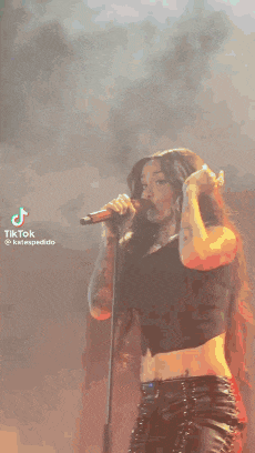 a woman is singing into a microphone on a stage while taking off her shirt .