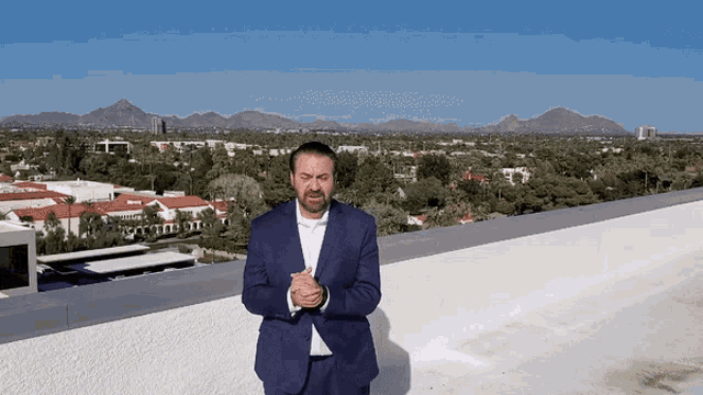 a man in a suit stands on a rooftop with his hands folded