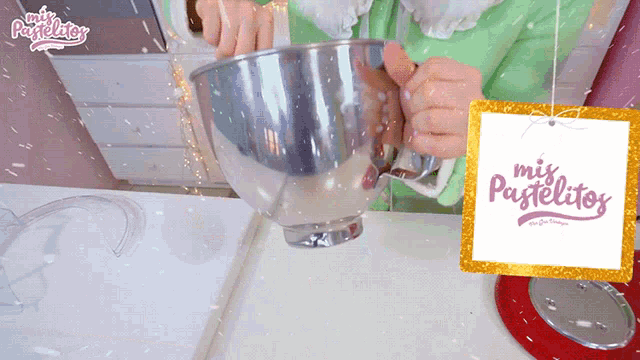 a person is mixing something in a metal bowl with a sign that says mis pastelitos