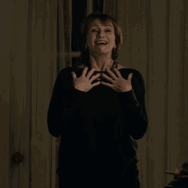 a woman wearing a black sweater and a necklace is smiling and clapping
