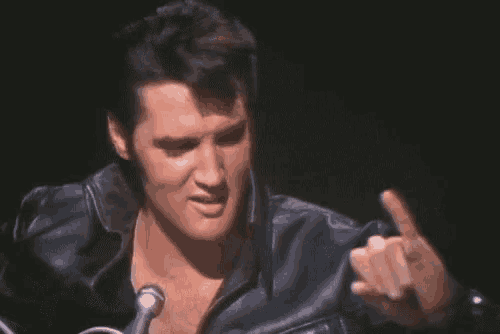elvis presley is wearing a leather jacket and giving a middle finger .