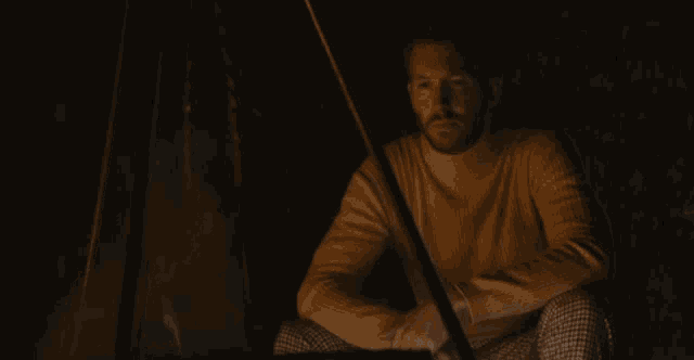 a man in a yellow sweater sits in front of a campfire at night