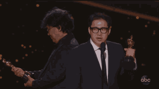 two men holding oscar trophies on a stage with abc written on the bottom
