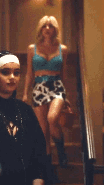 a woman in a blue bra and cow print skirt walking down stairs