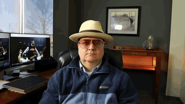 a man wearing a hat and sunglasses is sitting in front of a columbia jacket