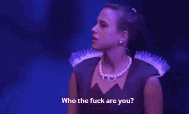 a woman in a black dress and pearl necklace is standing on a stage and talking to someone .