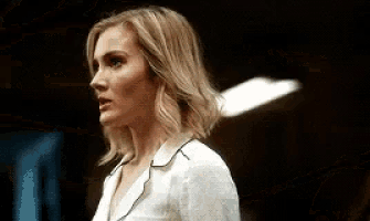 a woman in a white shirt is standing in a dark room looking at the camera .