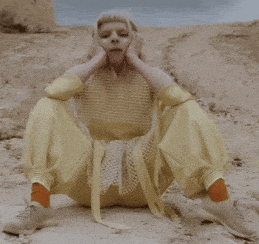 a woman wearing a yellow top and yellow pants is sitting in the sand