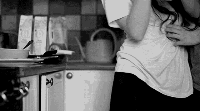 a black and white photo of a man and woman hugging in the kitchen .