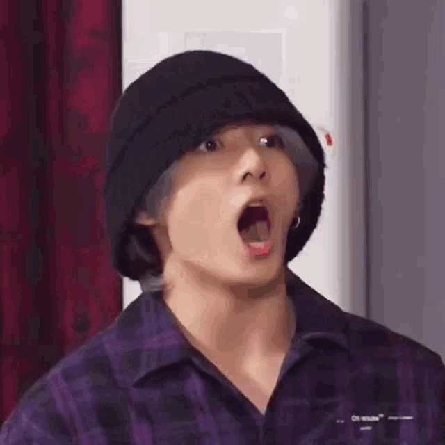 a young man wearing a black hat and a purple shirt is making a surprised face .