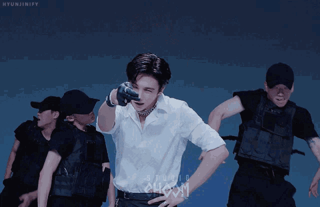 a man in a white shirt stands in front of a group of men in black vests and hats with the words studio show on the bottom