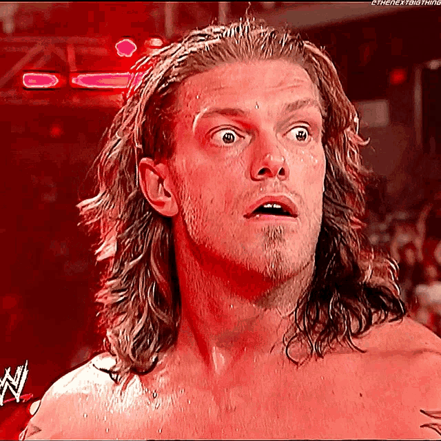 a shirtless wrestler with long hair and a beard looks surprised