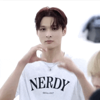 a young man wearing a white nerdy t-shirt making a heart shape with his hands