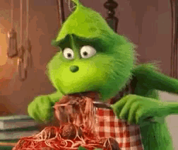 the grinch from the movie the grinch is eating spaghetti and meatballs with a fork and knife .