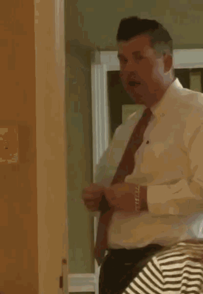 a man in a white shirt and red tie adjusts his tie in front of a mirror