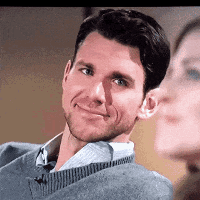 a man in a grey sweater is smiling while looking at a woman