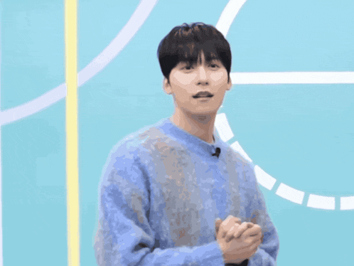 a man in a blue sweater is standing in front of a blue background