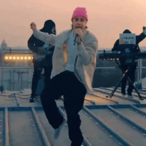 a man in a pink beanie is singing into a microphone on a rooftop