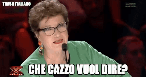 a woman wearing glasses and a green jacket is talking into a microphone and says che cazzo vuol dire