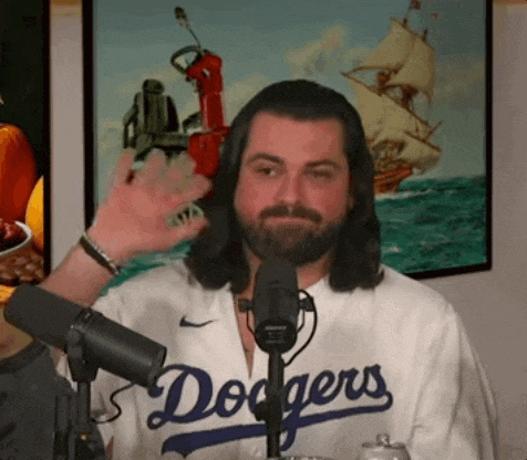 a man with long hair and a beard is wearing a dodgers jersey and waving at the camera .