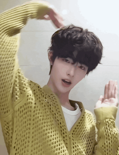 a young man wearing a yellow sweater is making a heart with his hands