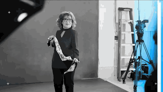 a woman wearing glasses is standing in front of a camera in a black and white photo .