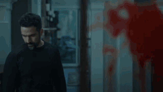 a man in a black shirt is standing in front of a bloody wall .