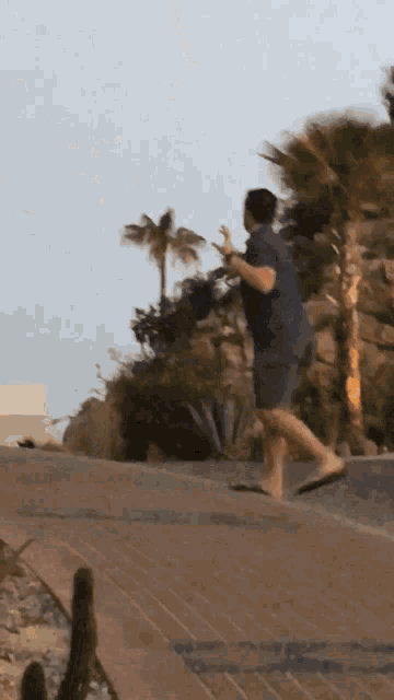 a man in a blue shirt and shorts is walking down a sidewalk with palm trees in the background