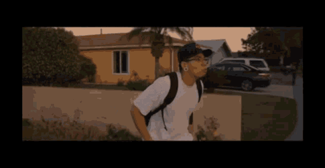 a man wearing a hat and a backpack is walking down a sidewalk in front of a house .