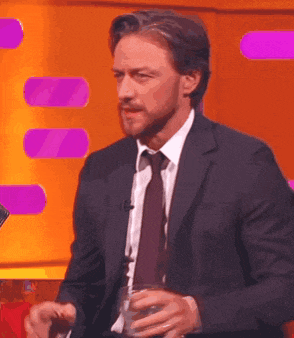 a man in a suit and tie is holding a glass of water while sitting in front of a microphone .