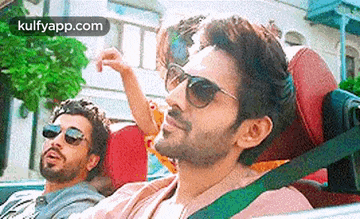 a man wearing sunglasses is sitting in the back seat of a car with two other men .