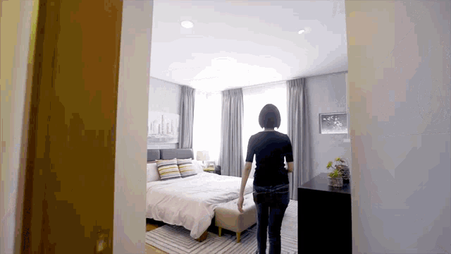 a woman is walking into a bedroom with a large bed and a dresser