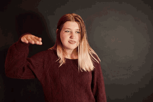 a woman in a maroon sweater is pointing her finger at the camera