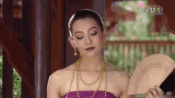 a woman in a purple dress is holding a fan and looking at something .