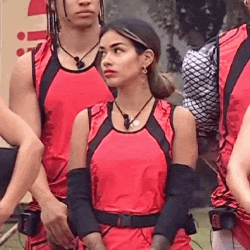 a woman in a red tank top and black gloves is standing next to a man in a red shirt .