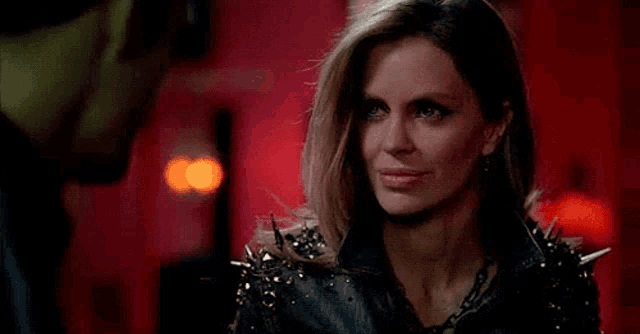 a woman wearing a black jacket with spikes on the shoulder is looking at the camera .