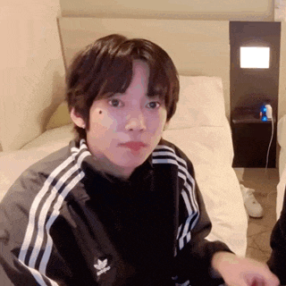 a young man is sitting on a bed wearing a black adidas jacket .