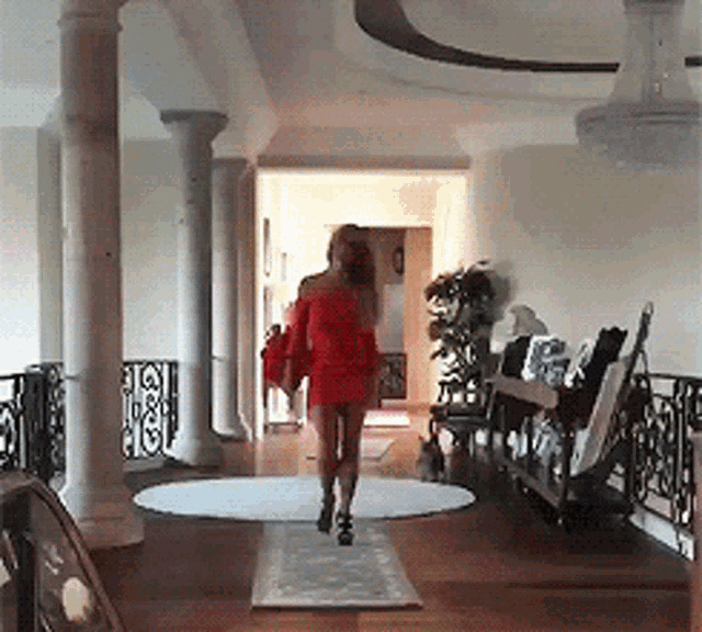 a woman in a red dress is walking down a hallway with columns