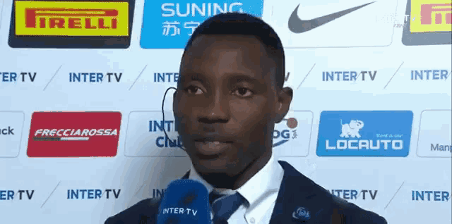 a man wearing a suit and tie is talking into a microphone in front of a wall with logos for nike and irelli