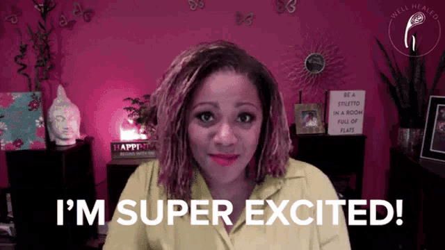 a woman says i 'm super excited while sitting in front of a pink wall