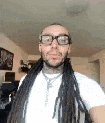 a man with dreadlocks and glasses is wearing a white shirt .