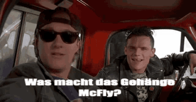 two men are sitting in a red truck and one of them is wearing sunglasses .