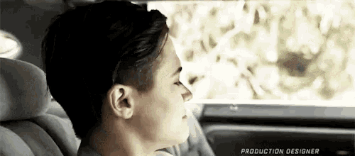a young man is sitting in the back seat of a car with the production designer written on the bottom of the screen