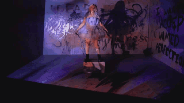 a woman in a white dress is standing in front of a wall that has graffiti on it that says " i wanted perfection "