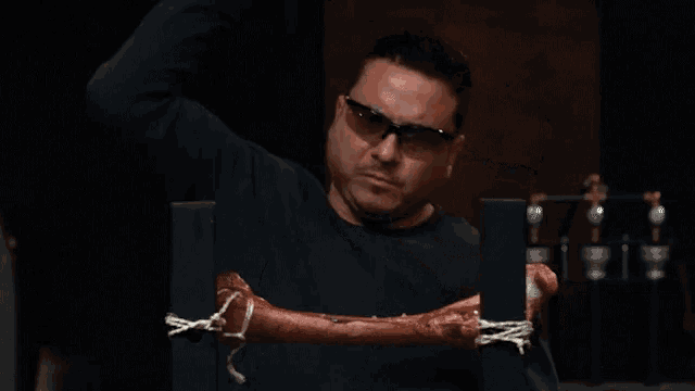 a man wearing glasses holds a piece of meat tied to a pole