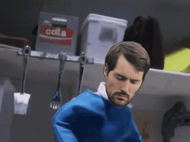 a man in a blue sweater is standing in front of a box that says cola