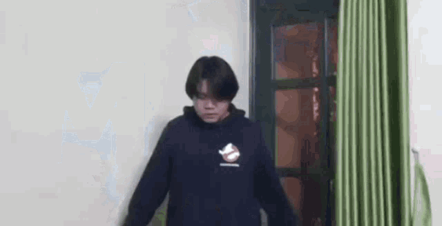a man in a black hoodie is standing in front of a door in a room .
