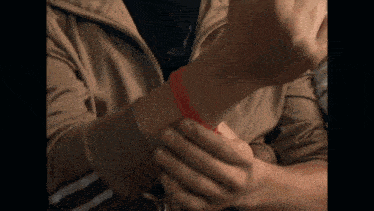 a person wearing a brown jacket has a red bracelet around their wrist